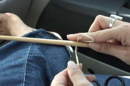A woman uses a wooden dowel in order to bend a piece of wire to make it fold almost in half.