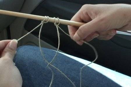 A string is looped over a dowel rod over a womans lap.
