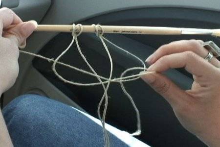 Two hands are holding a paintbrush with strings hanging from it.