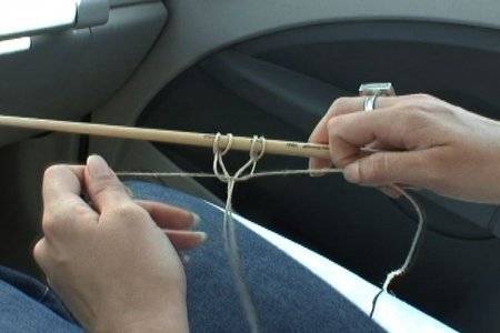 A pair of women's hands tying a knot with some string over a stick.