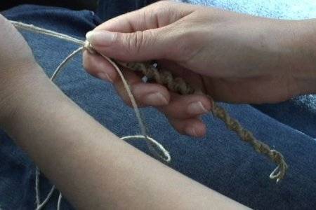 A person is braiding a string that they are holding in their hands.