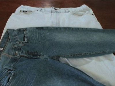 Two overlapping pairs of well-worn jeans, the top pair blue and the bottom pair white denim.