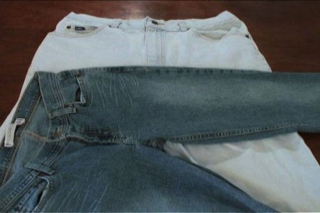 Two overlapping pairs of well-worn jeans, the top pair blue and the bottom pair white denim.