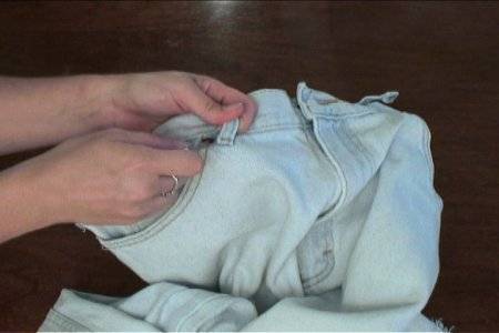 A pair of hands holding a pair of light colored jeans.