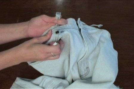 Woman removing pant belt loops with knife.