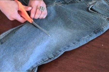 A person cutting a pair of jeans around the thigh area width-wise.