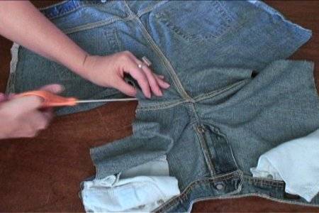 Hands using scissors to cut the crotch seam of a pair of denim bottoms turned inside-out.