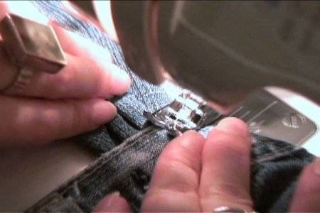Hands guiding denim fabric as a sewing machine stitches the edge.