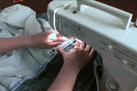 A person stitching a piece of cloth with a white sewing machine.