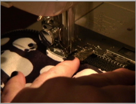 Person using a sewing machine to fasten a zipper to a piece of black fabric with white dots.