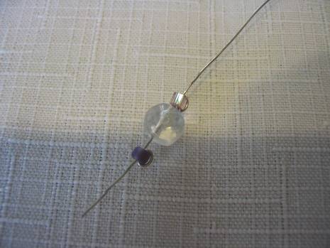 Thin piece of silver wire threaded with a large clear bead and two small silver beads.