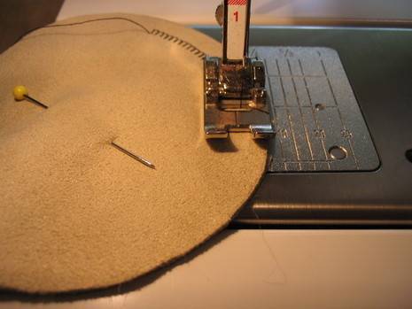 A sewing machine that is putting a stitch into a piece of brown cloth.