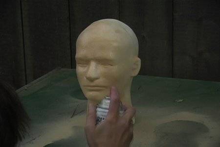 Rubber human face being molded on a metal stand by a person in a small booth.