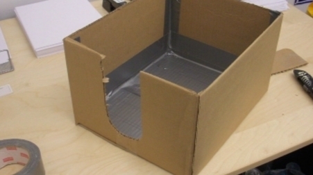 Cardboard box with cutout on one side and duct taped interior