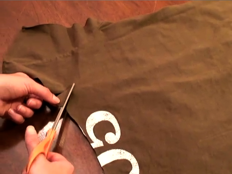 A brown colored t-shirt is being cut with a scissors.