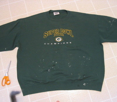 "A round neck green T-shirt on the tile floor with a scissor near it."