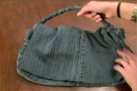 A purse made entirely from jean material held by a pair of hands.