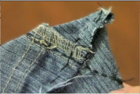 A hand holding the edge of some jean material with sewing on it.