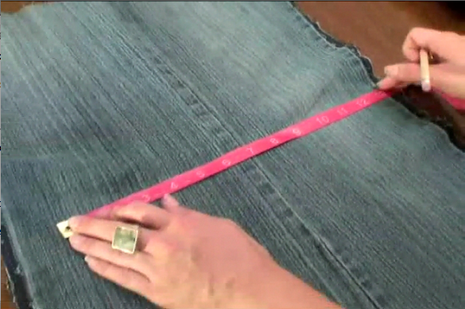 A pair of hands measuring some jean fabric with a tape measure ruler.