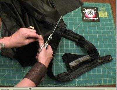 A man is cutting pieces off a black leather jacket.