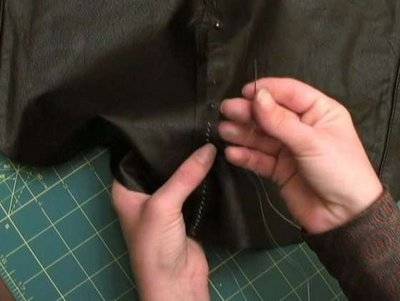 A person sewing black fabric with needle and tread.