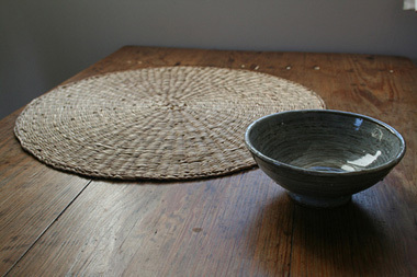 Circular shape table mat and bowl are on the wooden table.