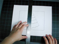 A pair of hands measuring a paper with a Christmas Tree drawn on it.
