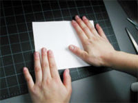 A pair of hands pressing on a flat piece of white paper.