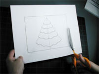 A pair of hands with a scissor cutting a large paper with a Christmas Tree figure on it.