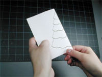 A person is holding the paper and how to make a christmas tree popup card.