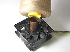 A computer fan next to a large spool of thread.