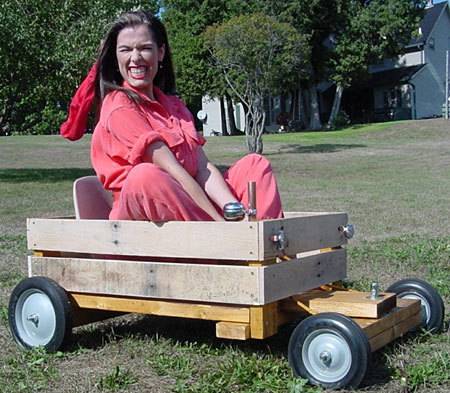 A woman in pink is sitting in a wooden wagon with wheels.