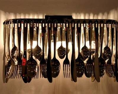 Various silverware items hung like a chandelier in front of a row of lights.