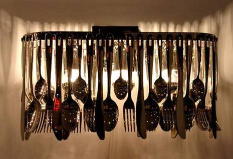 Various silverware items hung like a chandelier in front of a row of lights.