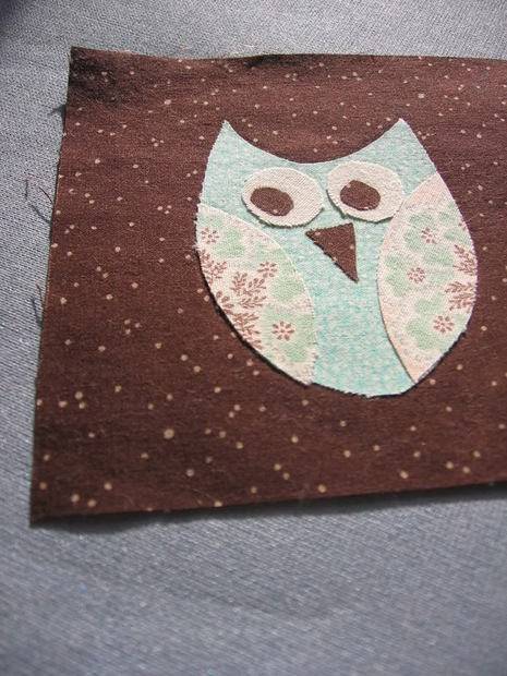 A light colored owl is on a brown fabric.