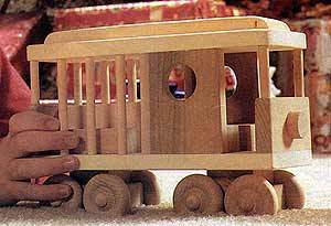 A person pushing a wooden trolley car on the carpet.