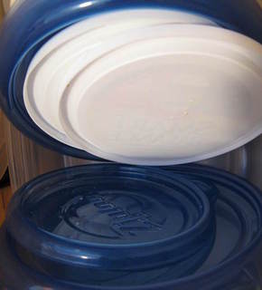 Stacks of solid white and transparent blue round plastic lids for containers.