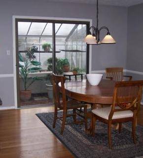 Interior view of a dining table and four chairs set on top of rug that covers hardwood floors and with a view to an outdoor enclosed porch.