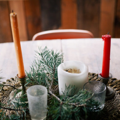 Candles are in candle holder and some leafy stems are placed in a circular table mat on dinning table.