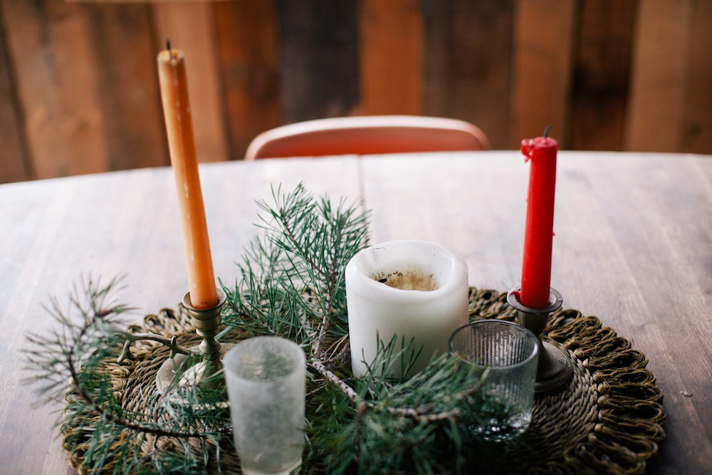 Candles are in candle holder and some leafy stems are placed in a circular table mat on dinning table.