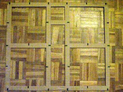 A large piece of cardboard with squares and rectangles cut into it, sitting on a wooden floor.