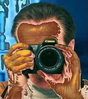 A person with paint on their hands and face holds a camera up to their eye to take a photo.