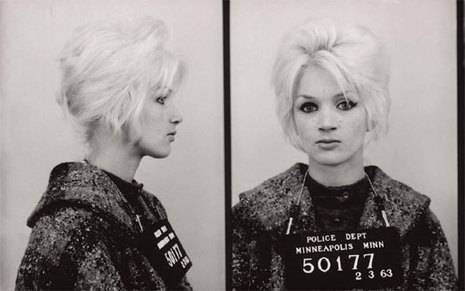 Two mugshots, one from the side and one from the front, of a light-haired woman wearing a coat with identifying plate hanging down from her neck.