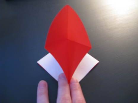 A piece of paper, red on one side and white on the other, being folded into a heart shaped envelope.