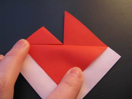 A person folding a piece of red paper.