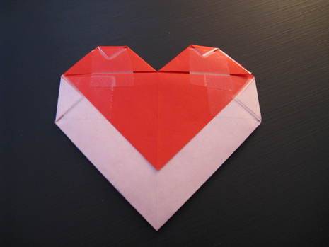 Red origami heart made out of an envelope resting on top of a black table.