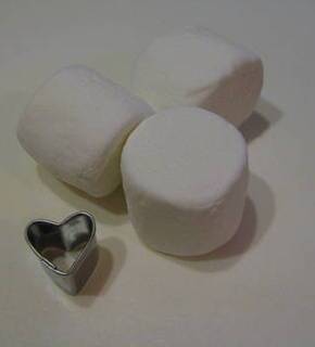 Marshmallows sitting next to a silver and black heart piece of metal.