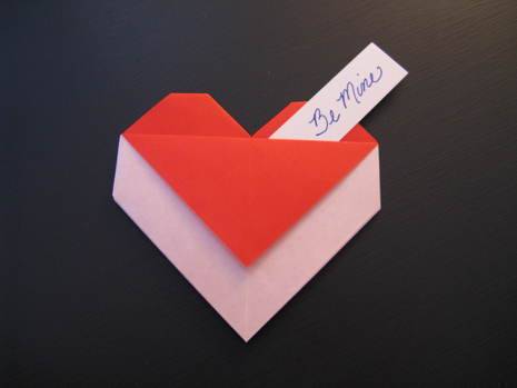 "A origami envelope in heartin shape is made using red and white paper".