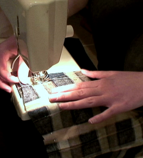 Two hands holding a piece of black and white material through a sewing machine.