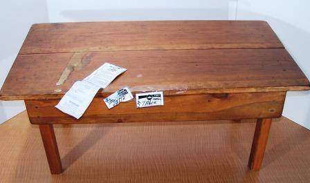 An old wooden desk with a seam in the middle and some scrap paper taped on one of the sides.
